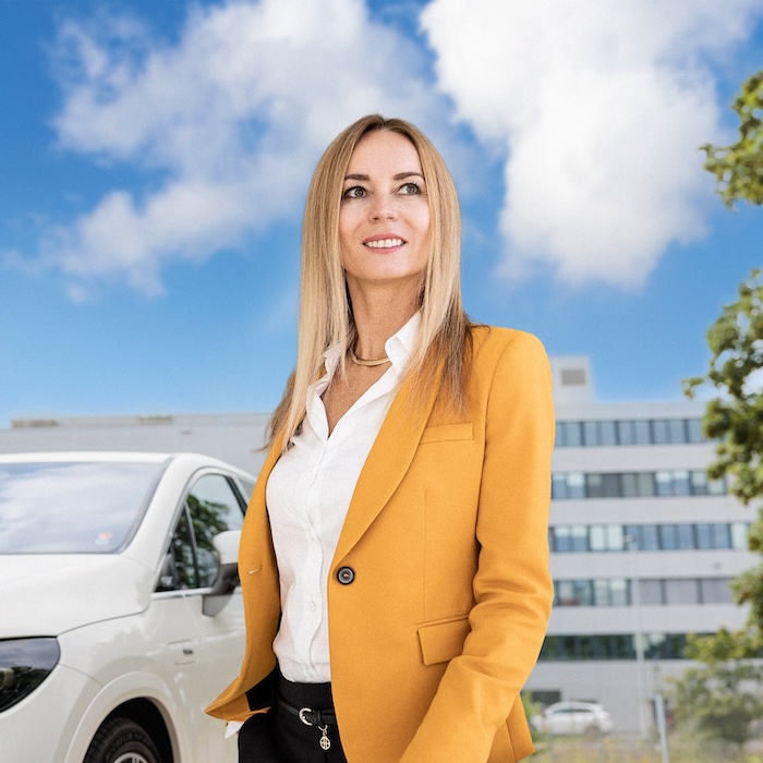 Woman in a yellow blazer standing outdoors and looking to the side with a blue sky in the background