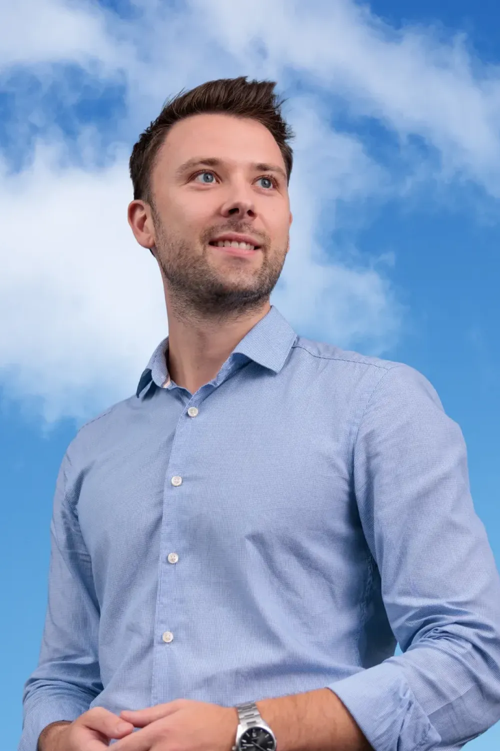 Man in a light blue shirt looking into the distance in front of a cloudy sky