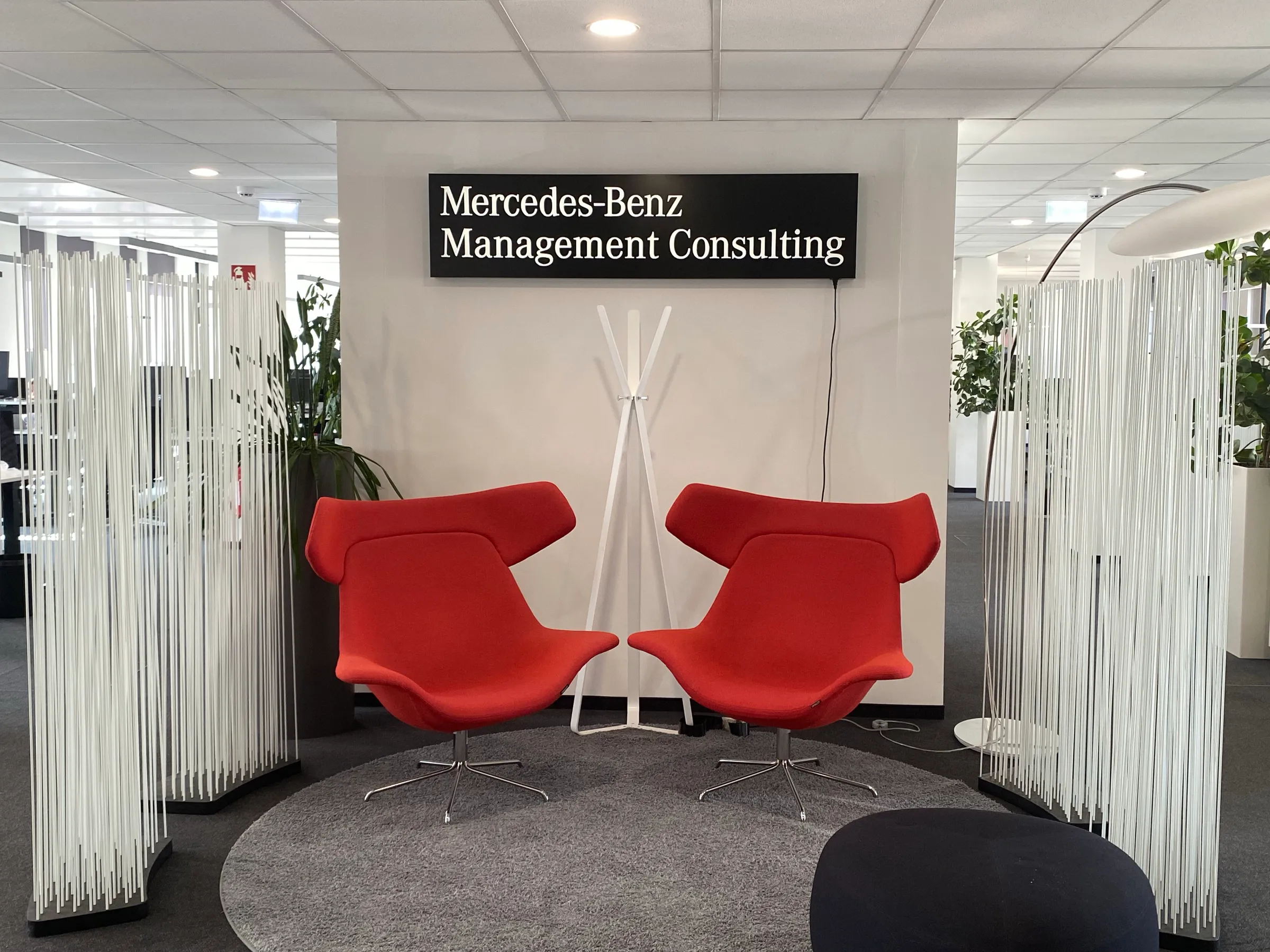 Two red lounge chairs in front of a Mercedes-Benz Management Consulting sign in the office